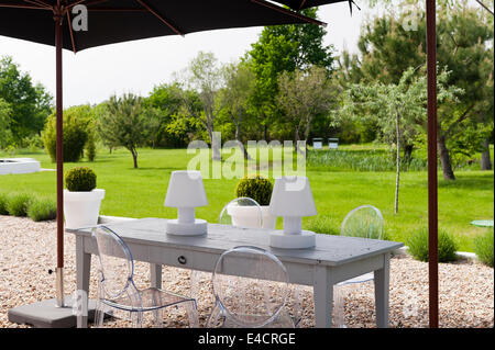 Garten Lichter auf Holztisch mit Philippe Starck Ghost Stühle unter Sonnenschirm im Garten Stockfoto