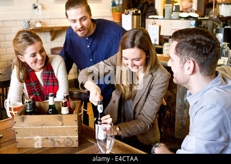 Junge Frau Eröffnung Flasche Bier, Freunde beobachten, Dorset, Bournemouth, England Stockfoto