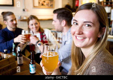 Junge Frau trinkt Bier im Pub, Freunde im Hintergrund, Dorset, Bournemouth, England Stockfoto