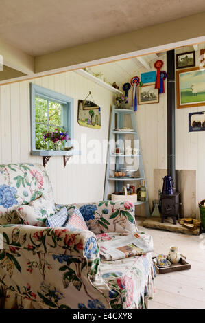 Ein floral gemusterten Sessel in einer gemütlichen Hirten-Hütte mit einem "Wendy" Kaminofen von windigen Schmiede Stockfoto