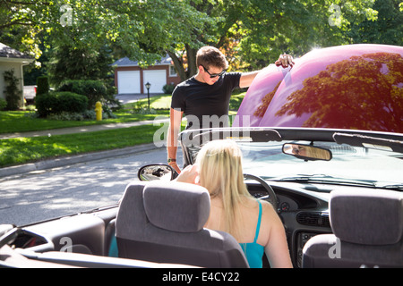 Ein junger Mann sieht unter der Haube des roten Cabrio als junge Frau in den Auto-Aufforderungen zur Unterstützung Stockfoto