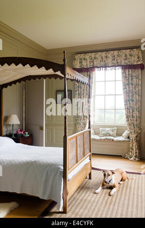 Ein Lutyens Schlafzimmereinrichtungen Bett im Schlafzimmer mit Colefax und Fowler Stock Länge Vorhänge. Die Wände sind in beige von Farrow und B gestrichen. Stockfoto