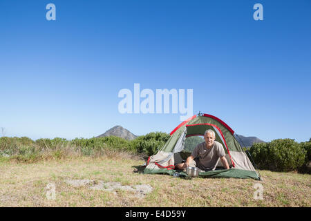 Glücklicher Camper auf Campingkocher außerhalb seines Zeltes Kochen Stockfoto