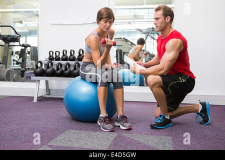 Personal Trainer mit Kunden sitzen auf Gymnastikball Hantel heben Stockfoto