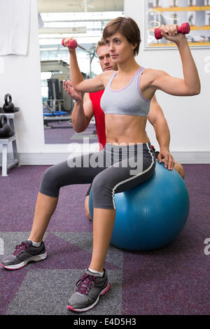 Personal Trainer mit Client Aufhebung Hanteln auf Gymnastikball Stockfoto