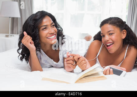 Mutter und Tochter Buch lesen und anhören von Musik zusammen auf Bett Stockfoto