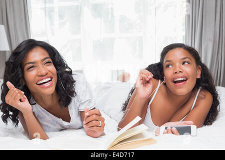 Mutter und Tochter Buch lesen und anhören von Musik zusammen auf Bett Stockfoto