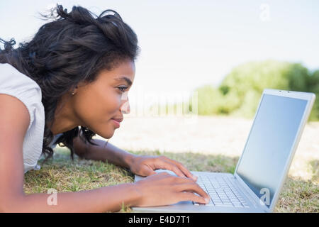 Lässige hübsche Frau liegend auf dem Rasen mit ihrem laptop Stockfoto
