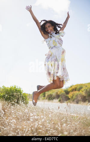 Gerne hübsche Frau sprang in geblümten Kleid Stockfoto