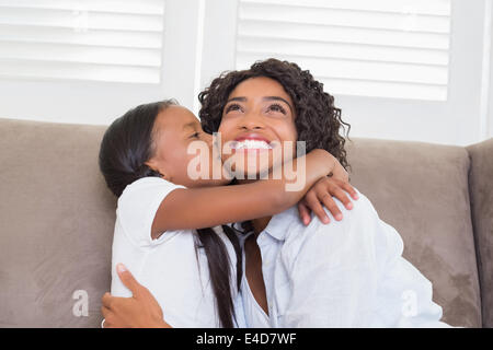 Hübsche Mutter mit ihrer Tochter ihre Wange küssen auf der Couch sitzen Stockfoto