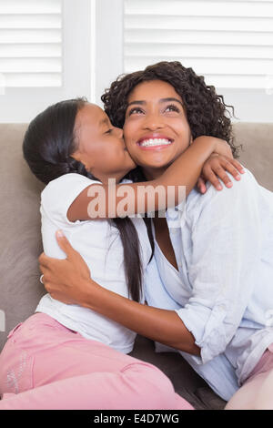 Hübsche Mutter mit ihrer Tochter ihre Wange küssen auf der Couch sitzen Stockfoto