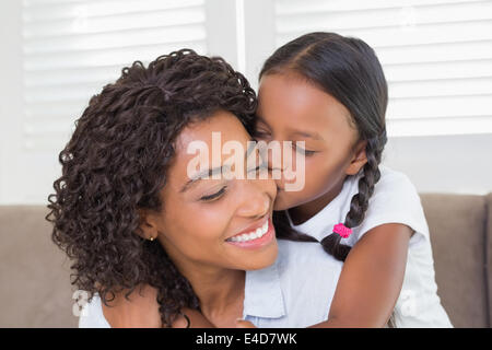 Hübsche Mutter mit ihrer Tochter ihre Wange küssen auf der Couch sitzen Stockfoto