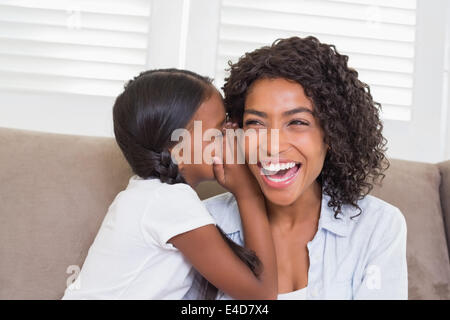 Hübsche Mutter mit ihrer Tochter ein Geheimnis Flüstern auf der Couch sitzen Stockfoto