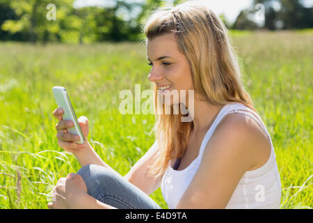 Hübsche Blondine sitzen auf dem Rasen eine SMS Stockfoto