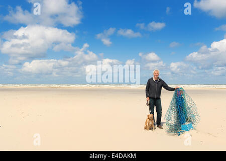 Mann mit Hund in der Nähe von Holzstange am Strand des niederländischen Wattenmeer Insel Terschelling Stockfoto