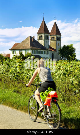 Frau auf Fahrrad vorbei an dem 15. Jahrhundert, romanische Kirche St. Peter und Paul in der klösterlichen Insel Reichenau Baden-Wurt Stockfoto