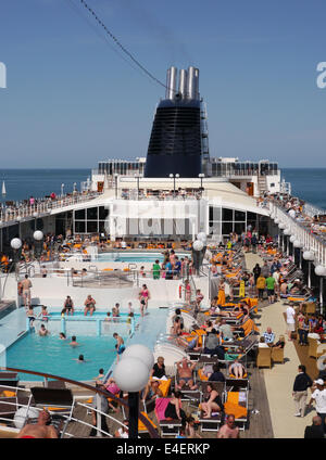 Das Oberdeck eine geschäftige Kreuzfahrtschiff mit Menschen rund um den Pool sitzen, an einem sonnigen Tag Stockfoto