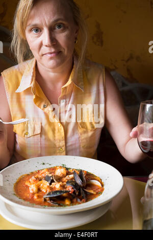 Reife kaukasischen Frau sitzt an einem Tisch Caciucco, ein italienischer Meeresfrüchte-Suppe mit Garnelen, Muscheln und Fisch, Essen und genießen Stockfoto