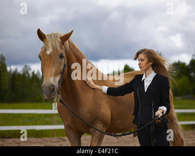 Schöne junge Frau und eine braune Hengst, bewölktem Himmel und Landschaft im Hintergrund Stockfoto