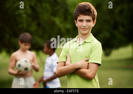 Porträt von Grundschulkind Kind Blick in die Kamera mit verschränkten Armen und die Kinder spielen Fußball im Hintergrund Stockfoto