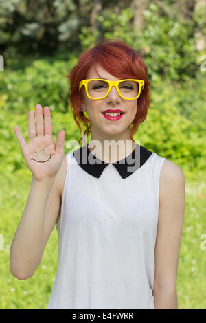 Niedliche Hipster Teenager Girl zeigt ein Smiley-Gesicht handgezeichnete auf ihre Handfläche, nett und fröhlich Stockfoto