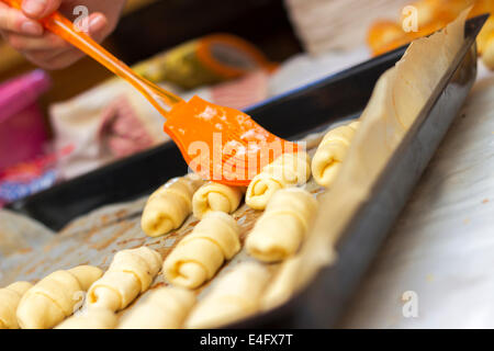 Baker setzen verquirltem Ei Mantel oben auf frisch Mini-Croissants nur vor dem Backen sie aufgerollt Stockfoto