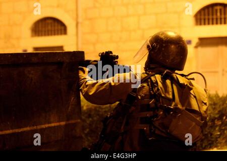 BETHLEHEM, WEST BANK Palästina - 2014/07/09-ein israelischer Soldat bekommt ein Tränengas-Behälter in eine Menge von palästinensischen Jugendlichen schussbereit. Für die acht Nacht hintereinander brachen intensiven Auseinandersetzungen in Bethlehem in der Nähe von Rachels Grab, auch bekannt als Prüfpunkt 300. In dieser Nacht warfen palästinensische Jugendlichen mit Steinen aus einer anderen Straße, die zu den militärischen Wartturm führt. Gewalt hat nicht aufgehört, seit letzter Woche Beerdigung von Muhammad Abu Khdeir und es gibt keine Anzeichen, die es in den kommenden Wochen sterben wird, ab. Seit Israels Eskalation und militärischen Einmarsch in Gaza genannt "Fels in der Brandung" Resenment in Richtung t Stockfoto