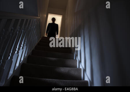 Silhouette eines Mannes stehen an der Spitze einer Treppe, Schatten an den Wänden des Lichts unter. Stockfoto