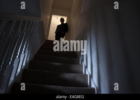 Silhouette eines Mannes lehnt an der Wand am oberen Ende einer Treppe, Schatten an den Wänden des Lichts unter. Stockfoto