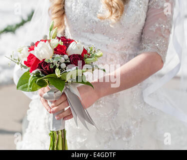 Eine Winter-Braut hält einen roten und weißen Blumenstrauß. Stockfoto