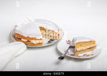 Victoria-Biskuit Eistee in weiß mit handgemachten Rosen auf einem Teller Kuchen auf einem Teller neben (44 44) Stockfoto