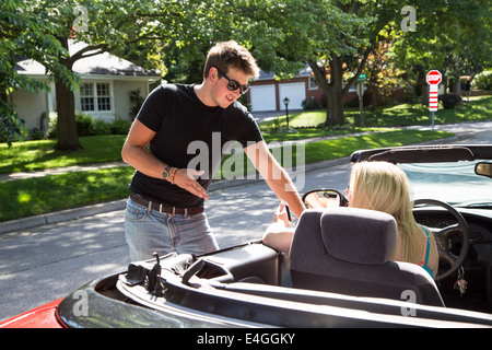 Ein junger Mann steht im Gespräch mit einer jungen Dame in einem roten Cabrio. Er kann ihr Wegbeschreibungen oder vielleicht fragen sie sich. Stockfoto