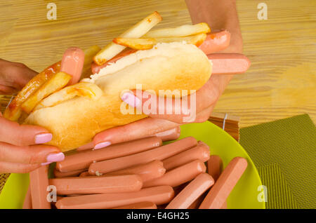Weibliche Hände halten Hotdog gefüllt mit viel Wurst und Pommes frites, eine ungesunde Lebensmittel-Konzept Stockfoto