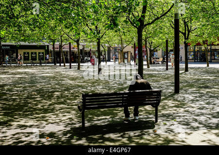 Ein Mann sitzt unter gefleckte Sonnenlicht. Stockfoto