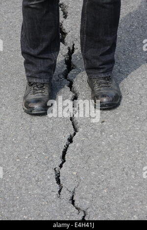 Eine Person steht über einen Riss verursacht durch einen Erdrutsch auf einer stillgelegten Straße auf Mam Tor, in der Nähe von CasteltonPeak Bezirk, Derbyshire, UK Stockfoto