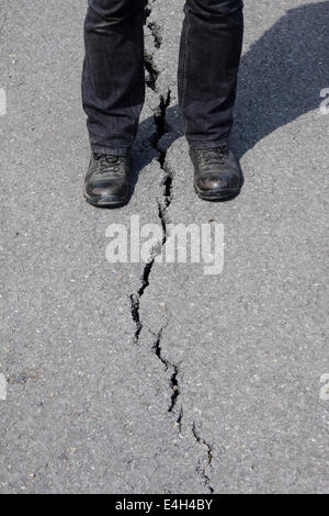 Eine Person steht über einen Riss verursacht durch einen Erdrutsch auf einer stillgelegten Straße auf Mam Tor, in der Nähe von CasteltonPeak Bezirk, Derbyshire, UK Stockfoto