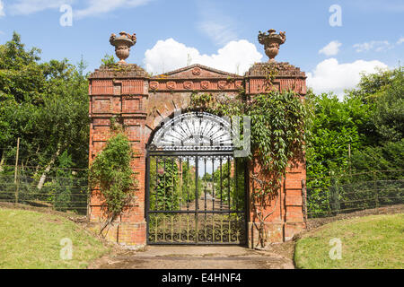 Mauerwerk Bogen und schwarzem Schmiedeeisen Schmiedeeisen Tor zum Walled Garden von Sandringham House, Norfolk, Großbritannien mit blauem Himmel und weißen Wolken Stockfoto