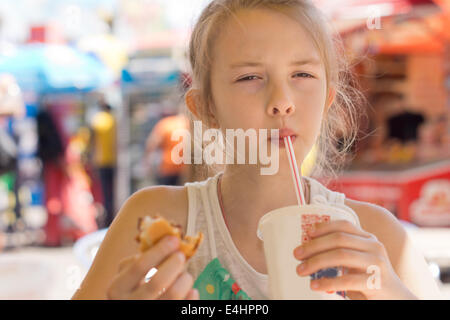 Durstige hungrige junge Mädchen eine Soda in einem Straßencafé schlürfen, wie sie einen Take-away Hamburger isst Stockfoto