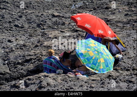 Menschen, die Schutz vor Wind und Sonne unter Sonnenschirmen in einer felsigen Senke Stockfoto