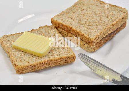 drei Scheiben Toast und Butter mit Messer auf weißen Teller, Nahaufnahme Stockfoto