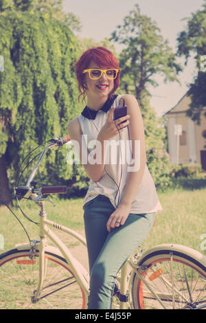 Hipster Teenager-Mädchen auf ihrem Oldtimer Fahrrad Musikhören auf ihrem lila smart Phone. Retro-Farben, getönten Bild Stockfoto