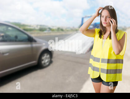 Frau am Telefon mit einem Reflektor Weste in der Nähe von ihr kaputtes Auto Stockfoto