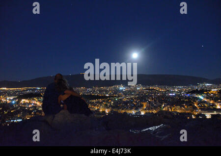 Athen, Griechenland. 12. Juli 2014. Ein paar sitzt auf Filopapou Hill Uhren der Vollmond über Bergen über der Stadt von Athen. Ein Supermoon tritt auf, wenn der Mond etwas näher an der Erde ist, als es in der Regel ist, und der Effekt am deutlichsten, ist wenn sie zur gleichen Zeit wie ein Vollmond auftritt. Bildnachweis: George Panagakis/Pacific Press/Alamy Live-Nachrichten Stockfoto