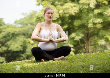 Porträt von weißen schöne schwangere Frau Yoga trainieren im Park sitzen auf dem Rasen, Lotus-position Stockfoto