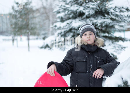 Junge in einem verschneiten Wald mit einem Schlitten Stockfoto