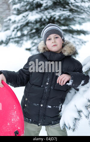 Junge in einem verschneiten Wald mit einem Schlitten Stockfoto