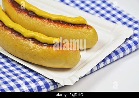 zwei gegrillte Würstchen mit Senf auf Pappteller mit blau-weiß karierte Serviette, Nahaufnahme Stockfoto