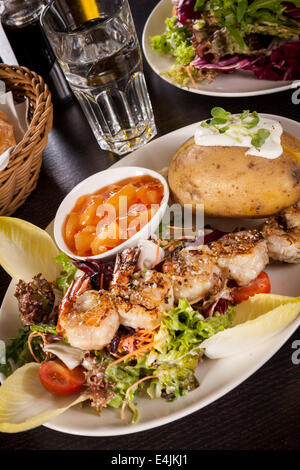 Gegrillte Garnelen mit grünem Blattgemüse Kopfsalat und Endivien Salat und eine Ofenkartoffeln mit Sauerrahm garniert serviert auf einem weißen Teller, c Stockfoto