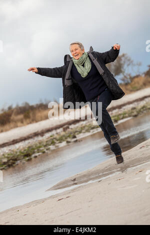 Beautiful senior Woman tummeln sich auf den Strand schreitende zusammen mit ausgebreiteten Armen und einem Lächeln der Wertschätzung, wie sie Natur genießt eine Stockfoto