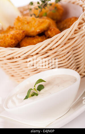 Knusprig gebratene Panierter Hähnchen-Nuggets in einem Weidenkorb diente als Fingerfood oder als Vorspeise mit einer cremigen Dip in einer Schüssel zusammen mit Stockfoto